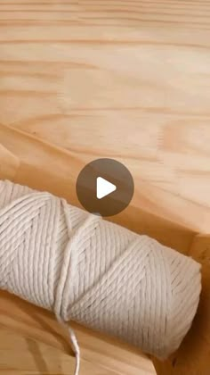 a roll of white yarn sitting on top of a wooden table next to a ball of string