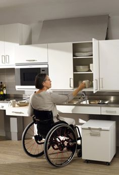 a woman in a wheel chair washing dishes at the kitchen sink and looking up into the sky