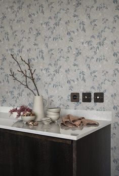 a vase with some flowers on top of a counter in a room that has blue wallpaper