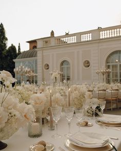 the table is set with white flowers and place settings for an elegant wedding reception in front of a large building