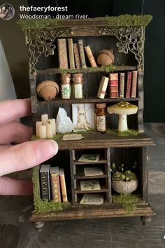 someone is holding a miniature book shelf with books on it and moss growing out of the shelves