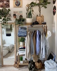 a room filled with clothes and plants next to a mirror on a wall above a bed