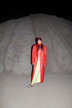 a woman in a red trench coat standing next to a pile of rocks at night