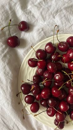 a white plate topped with lots of cherries on top of a cloth covered table