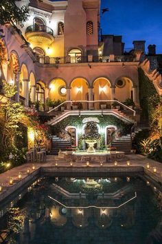 an outdoor swimming pool surrounded by greenery and lit up with candles in the evening