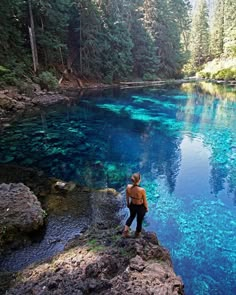 a woman standing on the edge of a cliff looking at blue water in a river