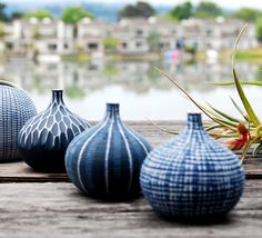 four vases are sitting on a wooden table near the water and houses in the background