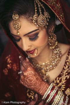 a woman in a red and gold bridal outfit with jewelry on her head, looking down