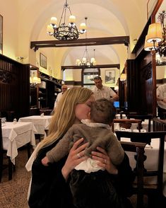 a woman holding a baby in her arms while sitting at a table with other people