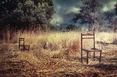 two empty chairs sitting in the middle of a field