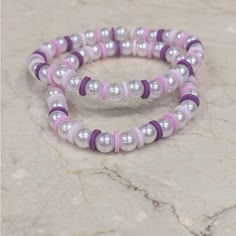 two bracelets with white and pink beads on a marble surface in front of a stone wall