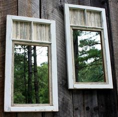 two mirrors are hanging on the side of a wooden building with trees reflected in them