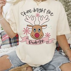 a woman sitting on the floor wearing a t - shirt that says, shine bright like rudolph