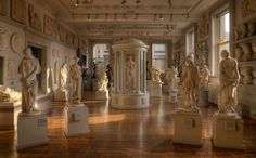 a room filled with lots of statues on display in front of large windows and wooden floors