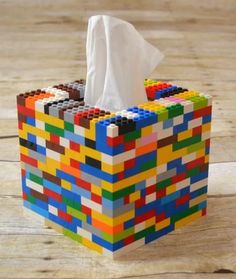 a tissue dispenser made out of lego blocks on a wooden floor with a white napkin in it