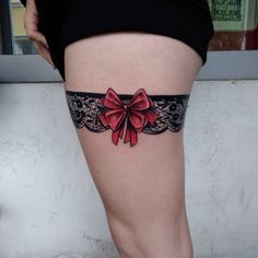 a woman's thigh with a red bow tattoo on her lower leg and black lace