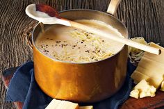 a wooden spoon sitting in a pot filled with soup next to sliced cheese and crackers