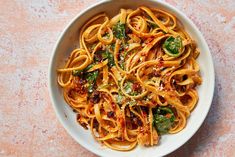 a white bowl filled with pasta and spinach on top of a pink tablecloth