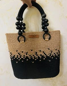 a hand holding a black and tan bag with beads on it's handles, hanging from a wall