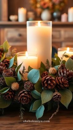 two candles are lit on a table with evergreen leaves and pine cones around the candle