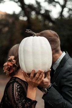 a man and woman holding up a white pumpkin in front of their face while they both look at each other