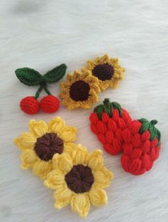 three crocheted strawberries and two sunflowers on a white furnishing