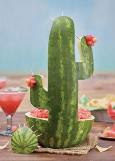 a watermelon cactus sitting on top of a wooden table next to two cocktail glasses