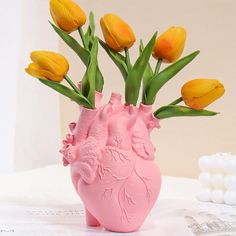 a pink vase with yellow tulips sticking out of it's heart shape