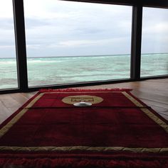 a red rug sitting on top of a wooden floor in front of large windows overlooking the ocean