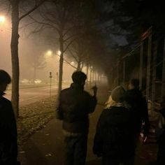 people standing on the sidewalk at night in the foggy city street with no cars