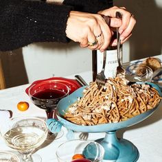 a person is cutting into some food on a table with wine glasses and other dishes