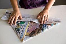 a young child is making a paper boat out of newspaper strips on a white table