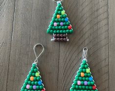 three beaded christmas tree ornaments on a wooden table