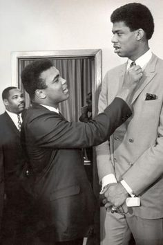 two men in suits standing next to each other and one is adjusting the tie on another man's suit