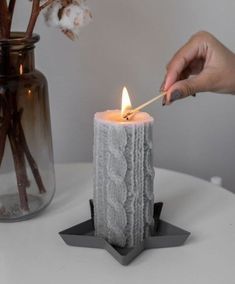 a person lighting a candle on top of a table next to a vase with cotton flowers