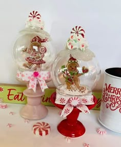 two snow globes sitting on top of a table next to a mug and candy cane