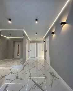 an empty room with white marble floors and lights on the ceiling, along with recessed lighting