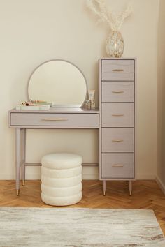 a dresser with a mirror, stool and round mirror on top of it next to a white rug