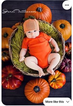 a baby wearing an orange shirt and hat sitting in a basket surrounded by pumpkins