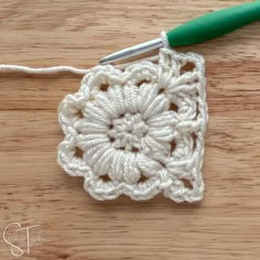 the crochet square is being worked on by a green handled needle and thread