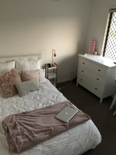 a laptop computer sitting on top of a bed next to a white dresser and window