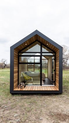 a small cabin with glass walls and wooden flooring in the middle of a field