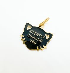 a black and gold cat shaped pendant with the words silently judging you written on it