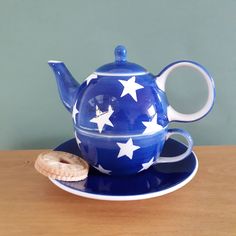 a blue teapot with white stars on it sitting on a saucer next to a cookie