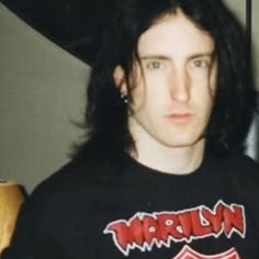 a man with long hair wearing a black t - shirt and looking at the camera