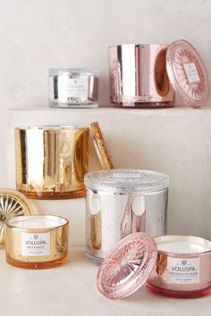 several different types of candles and containers on a shelf in a room with white walls