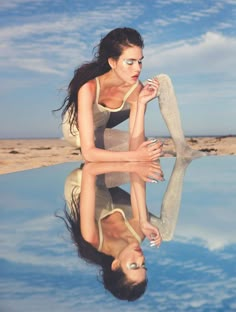 a woman in a bathing suit leaning on another woman's leg with her reflection in the water