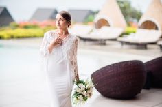 a woman in a white dress holding a bouquet and standing next to a swimming pool