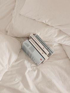 a stack of books sitting on top of a bed covered in white sheets and pillows