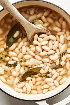 beans are being cooked in a pot with a wooden spoon on the side and green leaves sticking out of it